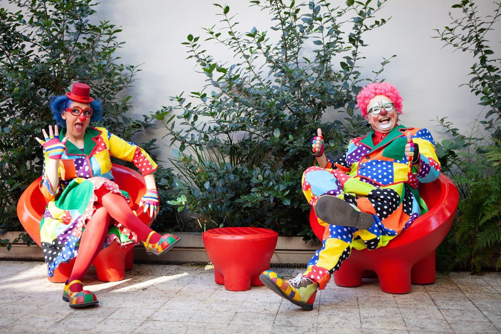 Deux clowns en costumes colorés assis sur des fauteuils rouges