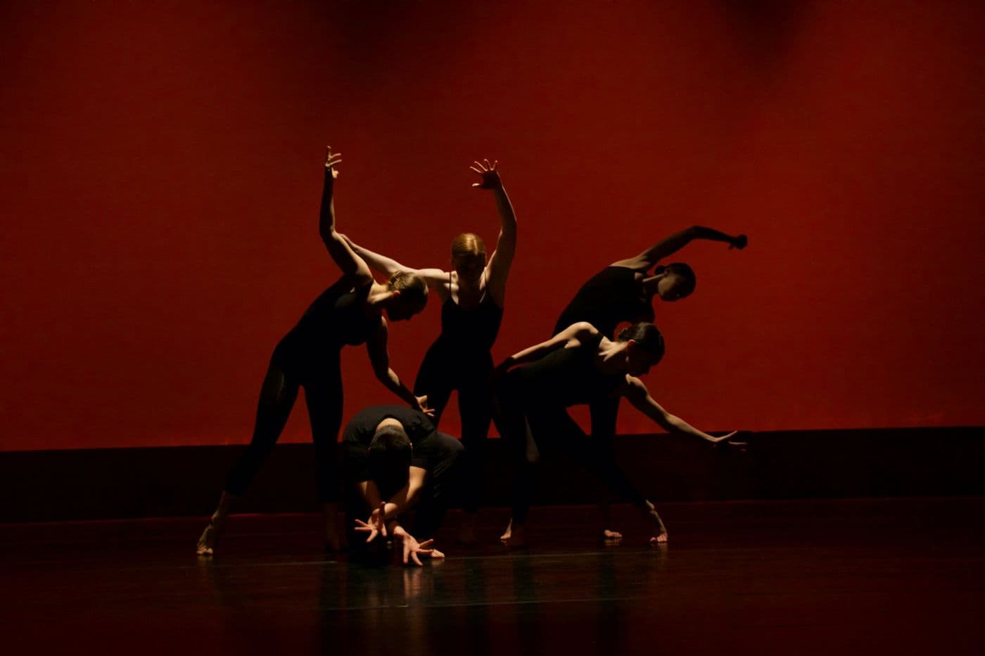 Cinq danseurs en silhouette sur une scène éclairée en rouge