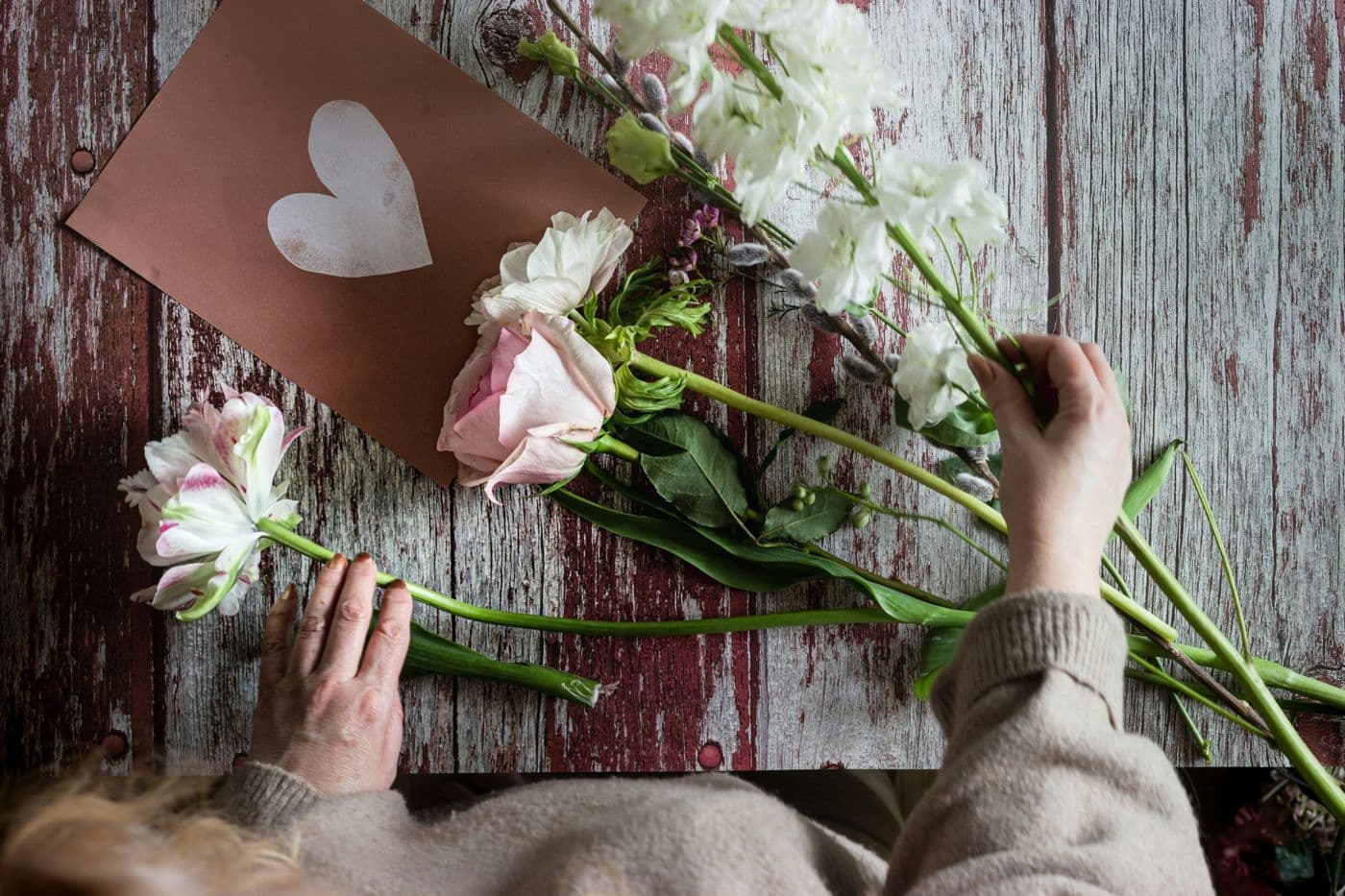 Fleuriste qui compose un bouquet de roses et de fleurs blanches sur une table en bois